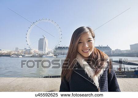 Portrait of happy young woman standing against London Eye at London, England, UK View Large Photo Image Stock Photography - Portrait of happy young woman standing against London Eye at London, England, UK. Fotosearch