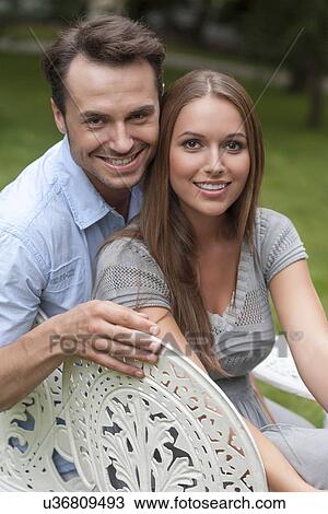 Portrait of loving young couple sitting on chairs in park View Large Photo Image Stock Image - Portrait of loving young couple sitting on chairs in park. Fotosearch