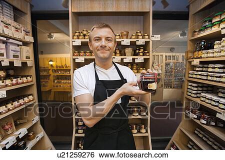 Stock Photograph - Portrait of mid adult salesman holding jar of jam in grocery store. Fotosearch