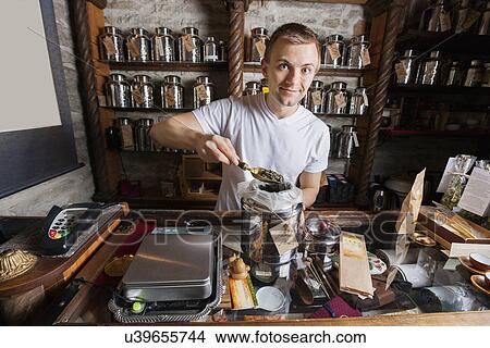 Picture - Portrait of salesman scooping tea from container at store. Fotosearch