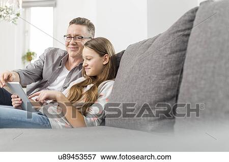 Portrait of smiling father assisting daughter in using digital tablet on sofa at home View Large Photo Image Stock Photo - Portrait of smiling father assisting daughter in using digital tablet on sofa at home. Fotosearch