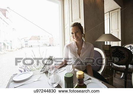 Stock Image - Portrait of smiling female customer sitting at restaurant table. Fotosearch