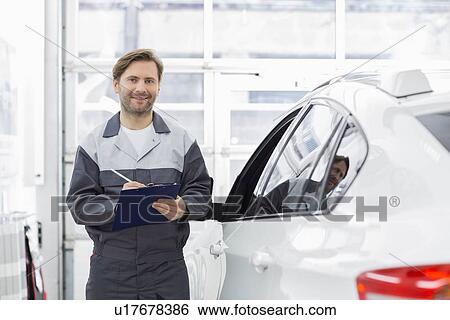 Portrait of smiling male automobile mechanic holding clipboard while standing by car in repair shop View Large Photo Image Stock Photograph - Portrait of smiling male automobile mechanic holding clipboard while standing by car in repair shop. Fotosearch