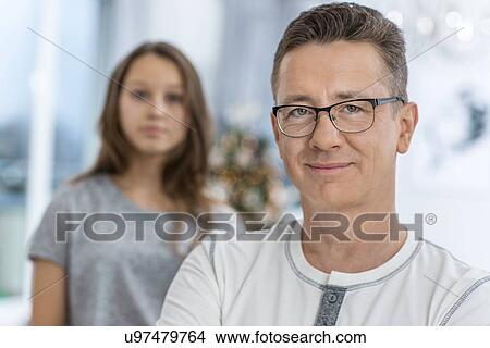 Picture - Portrait of smiling man with daughter standing in background at home. Fotosearch