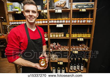 Stock Image - Portrait of smiling salesperson holding jar in supermarket. Fotosearch
