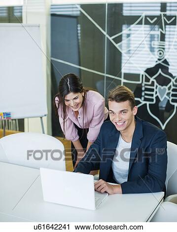 Portrait of smiling young businessman with female colleague using laptop at table in office View Large Photo Image Stock Image - Portrait of smiling young businessman with female colleague using laptop at table in office. Fotosearch