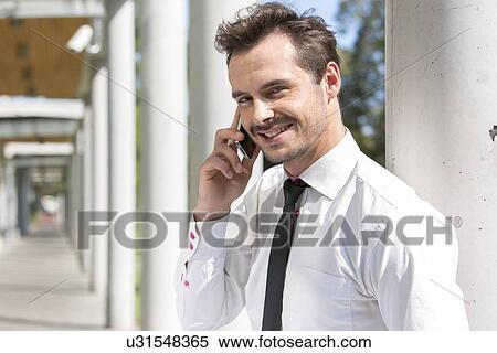 Portrait of smiling young businessman using cell phone outside office View Large Photo Image Stock Photography - Portrait of smiling young businessman using cell phone outside office. Fotosearch