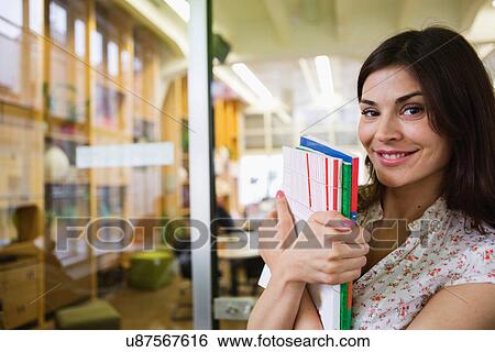 Stock Photograph - Portrait of smiling young businesswoman with books in office. Fotosearch