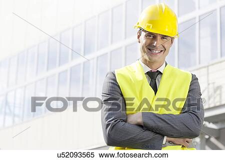 Stock Photography - Portrait of smiling young male architect standing arms crossed outside office building. Fotosearch