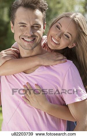Portrait of smiling young man being embrace by woman in park View Large Photo Image Stock Photo - Portrait of smiling young man being embrace by woman in park. Fotosearch