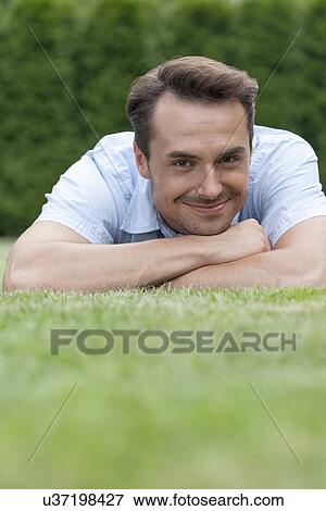 Portrait of smiling young man lying on grass in park View Large Photo Image Stock Photo - Portrait of smiling young man lying on grass in park. Fotosearch