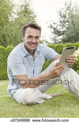 Stock Photograph - Portrait of smiling young man using tablet computer in park. Fotosearch