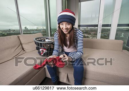 Stock Photo - Portrait of smiling young woman doing laundry work in living room at home. Fotosearch