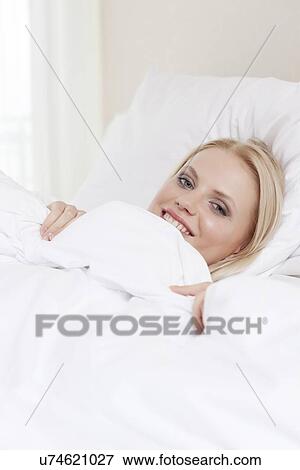 Portrait of smiling young woman lying in bed View Large Photo Image Stock Photo - Portrait of smiling young woman lying in bed. Fotosearch