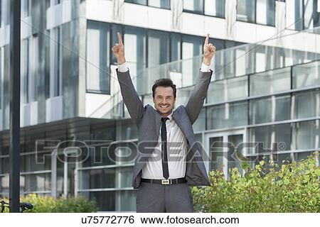 Stock Photograph - Portrait of successful businessman pointing upwards outside office. Fotosearch