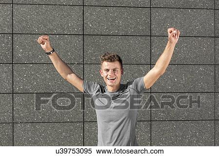 Stock Photography - Portrait of successful male jogger with clenched fist against tiled wall. Fotosearch