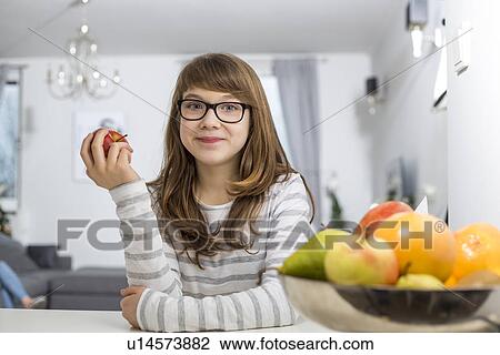 Stock Image - Portrait of teenage girl holding apple at home. Fotosearch