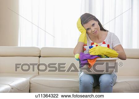 Portrait of tired woman with basket of cleaning supplies sitting on sofa at home View Large Photo Image Stock Image - Portrait of tired woman with basket of cleaning supplies sitting on sofa at home. Fotosearch