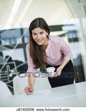 Portrait of young businesswoman holding coffee at desk in office View Large Photo Image Stock Photograph - Portrait of young businesswoman holding coffee at desk in office. Fotosearch