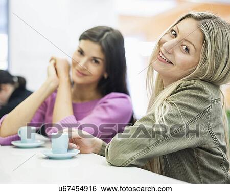 Stock Photograph - Portrait of young businesswomen smiling at cafeteria table. Fotosearch
