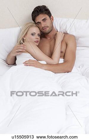 Stock Image - Portrait of young couple embracing in bed. Fotosearch