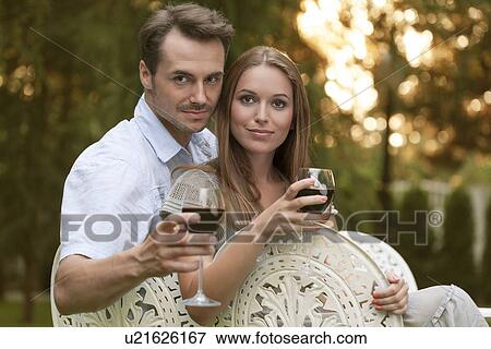 Portrait of young couple having red wine on chairs in park View Large Photo Image Stock Photo - Portrait of young couple having red wine on chairs in park. Fotosearch