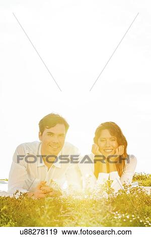 Portrait of young couple lying on grass against clear sky View Large Photo Image Stock Photo - Portrait of young couple lying on grass against clear sky. Fotosearch