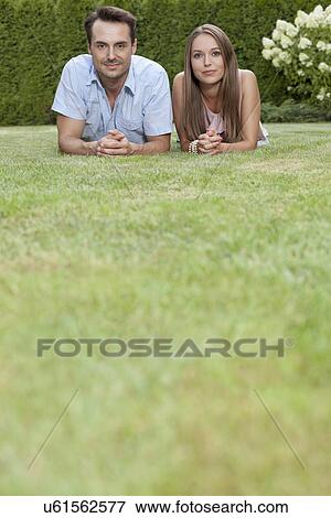 Stock Photo - Portrait of young couple lying side by side on grass in park. Fotosearch