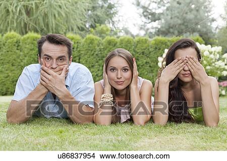 Portrait of young friends covering mouth, ears and eyes in park View Large Photo Image Picture - Portrait of young friends covering mouth, ears and eyes in park. Fotosearch