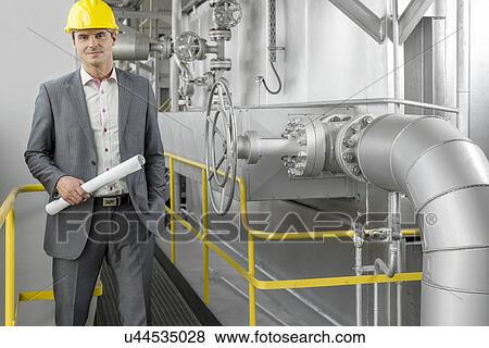 Portrait of young male architect holding blueprint by machinery at industry View Large Photo Image Stock Photo - Portrait of young male architect holding blueprint by machinery at industry. Fotosearch