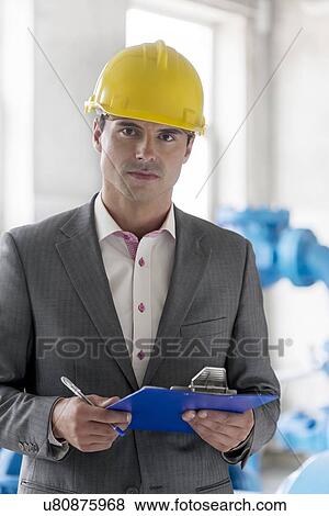 Stock Photo - Portrait of young male supervisor holding clipboard in industry. Fotosearch
