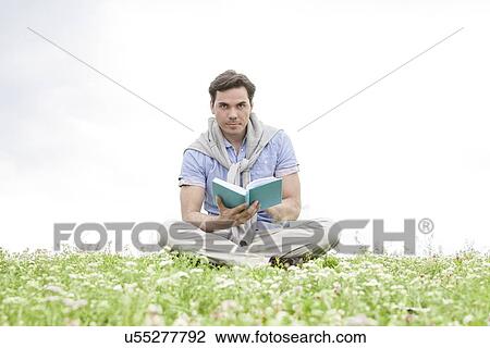 Portrait of young man reading book while sitting on grass against sky View Large Photo Image Stock Image - Portrait of young man reading book while sitting on grass against sky. Fotosearch