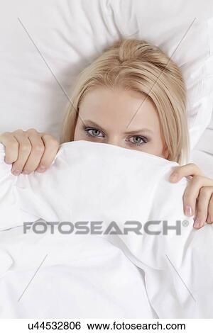 Stock Photograph - Portrait of young woman covering face with bed sheet. Fotosearch
