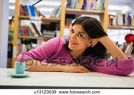 Stock Photo - Portrait of young woman with coffee on desk in library. Fotosearch
