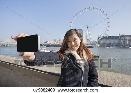 Portrait woman taking self portrait through cell phone against London Eye at London, England, UK View Large Photo Image Stock Photo - Portrait woman taking self portrait through cell phone against London Eye at London, England, UK. Fotosearch