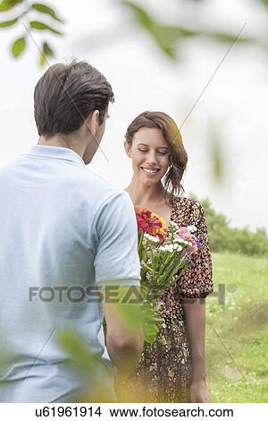 Picture - Rear view man giving flowers to woman in park. Fotosearch