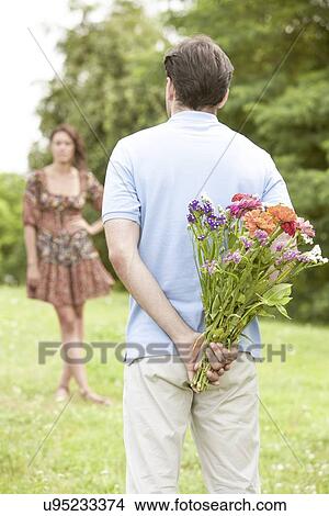 Rear view man surprising woman with flowers in park View Large Photo Image Picture - Rear view man surprising woman with flowers in park. Fotosearch