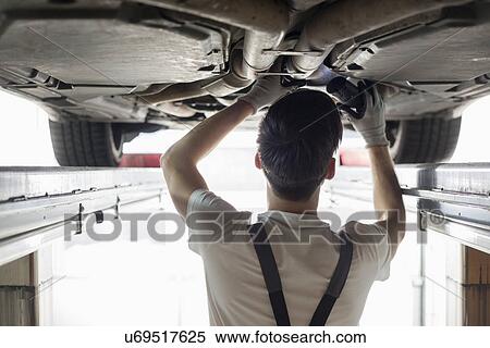 Stock Photography - Rear view of automobile mechanic examining car in workshop. Fotosearch