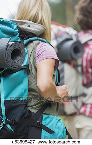 Stock Photo - Rear view of female hiker carrying backpack with man in background outdoors. Fotosearch