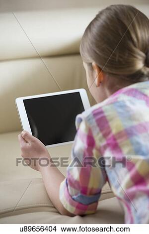 Picture - Rear view of girl using tablet PC at home. Fotosearch
