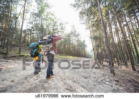 Stock Photograph - Rear view of hiking couple holding hands while walking in forest. Fotosearch