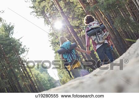 Rear view of hiking couple holding hands while walking in forest View Large Photo Image Stock Photography - Rear view of hiking couple holding hands while walking in forest. Fotosearch