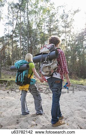 Stock Image - Rear view of hiking couple with backpacks walking in forest. Fotosearch