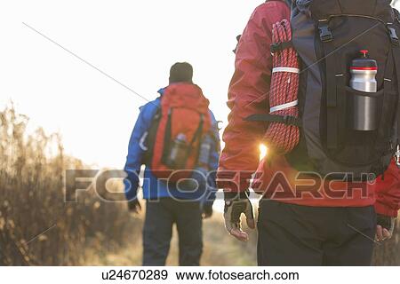 Stock Photo - Rear view of male backpackers walking in field. Fotosearch