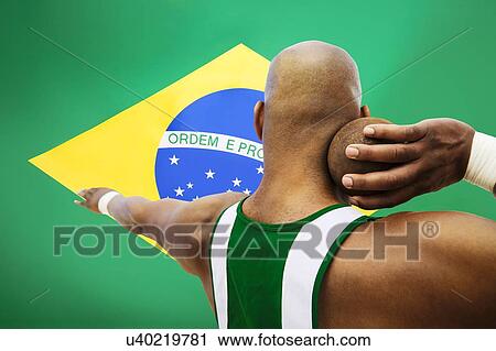 Stock Image - Rear view of male shot putter aiming against Brazilian flag. Fotosearch