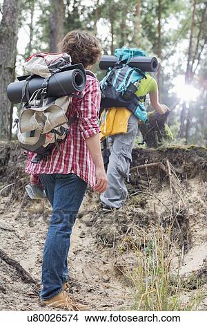 Picture - Rear view of man watching female hiker climbing cliff in forest. Fotosearch