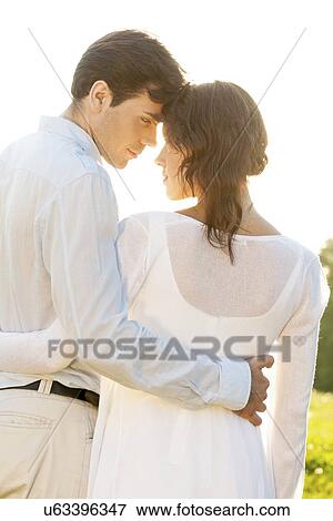 Stock Photo - Rear view of romantic couple standing arms around against clear sky. Fotosearch