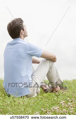 Rear view of thoughtful young man sitting on grass against sky View Large Photo Image Stock Image - Rear view of thoughtful young man sitting on grass against sky. Fotosearch