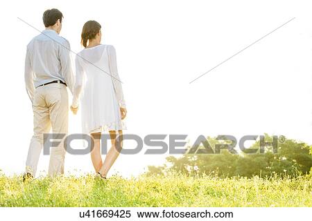 Rear view of young couple holding hands in park against clear sky View Large Photo Image Stock Photography - Rear view of young couple holding hands in park against clear sky. Fotosearch