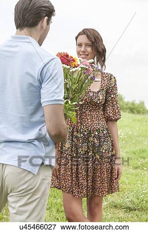 Rear view young man giving flowers to girlfriend in park View Large Photo Image Stock Photo - Rear view young man giving flowers to girlfriend in park. Fotosearch